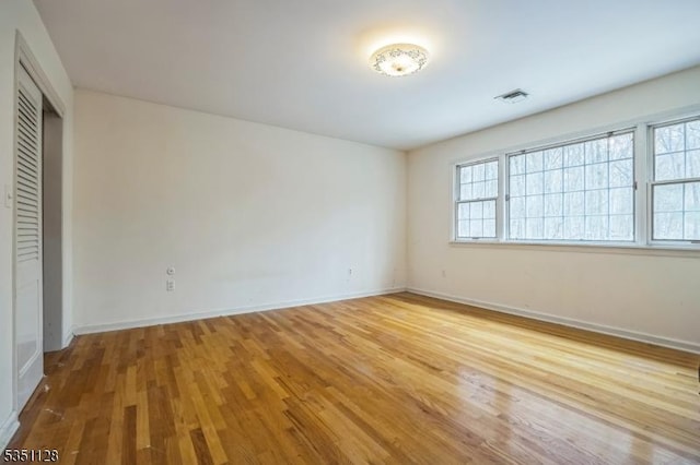 unfurnished bedroom featuring a closet, wood finished floors, visible vents, and baseboards