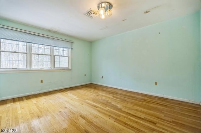 empty room with baseboards, a chandelier, wood finished floors, and visible vents