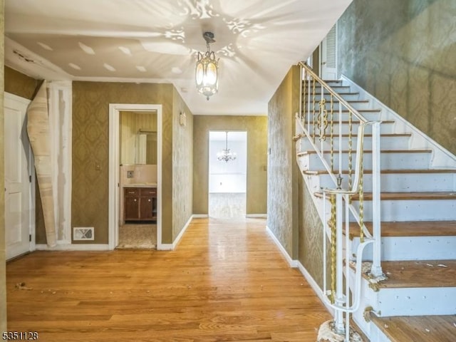 hall with stairway, wood finished floors, wallpapered walls, an inviting chandelier, and baseboards