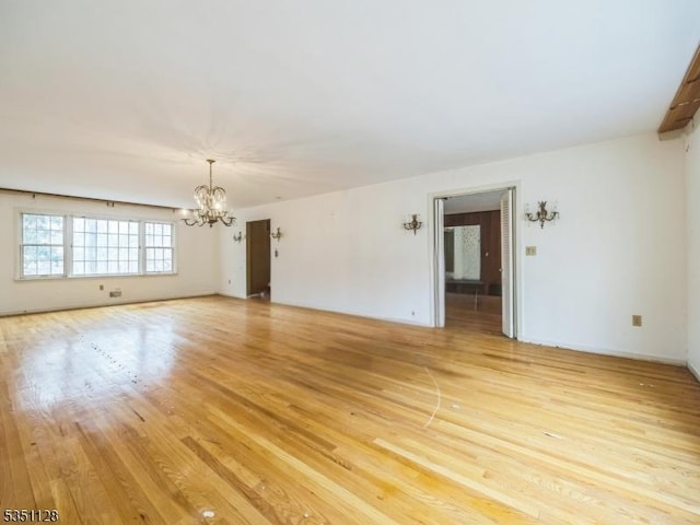 unfurnished living room with a chandelier, light wood-style flooring, and baseboards