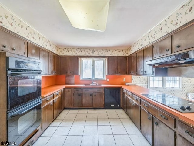 kitchen with wallpapered walls, under cabinet range hood, light countertops, a sink, and black appliances