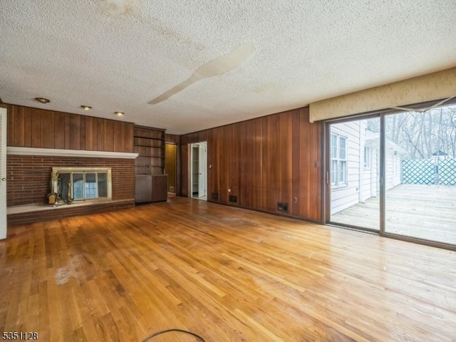 unfurnished living room featuring a fireplace, wood finished floors, a textured ceiling, and wood walls