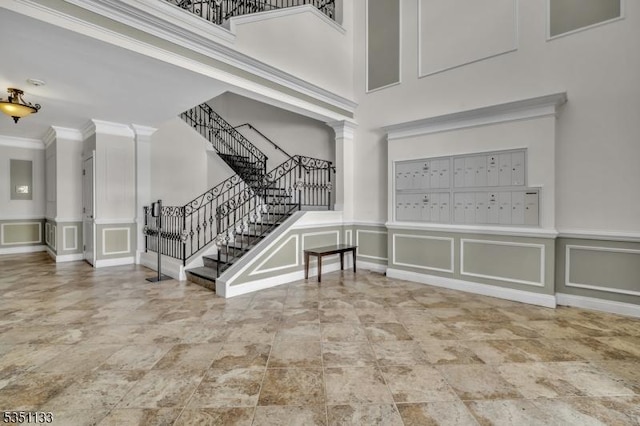 foyer with a decorative wall, ornamental molding, a towering ceiling, stairway, and mail area