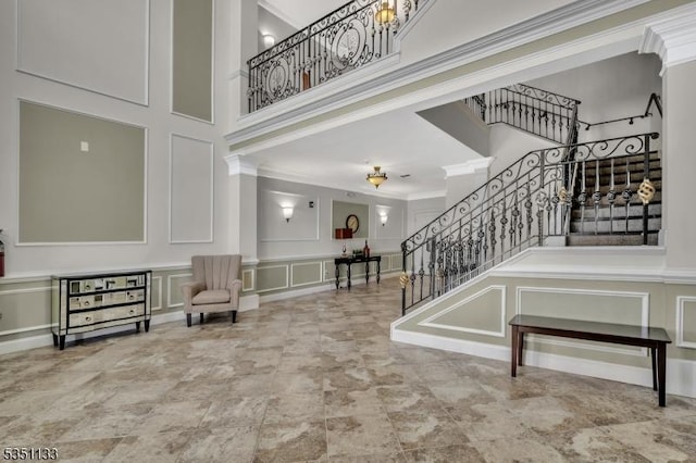 foyer entrance with a decorative wall, stairway, a towering ceiling, and crown molding
