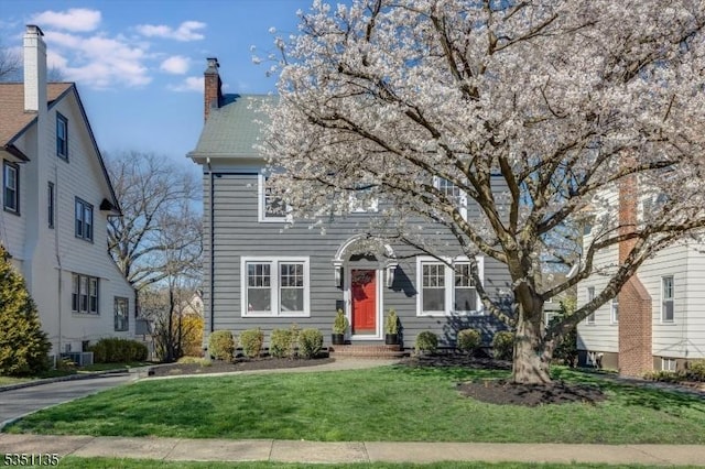 view of front facade featuring central AC unit, a front lawn, and a chimney