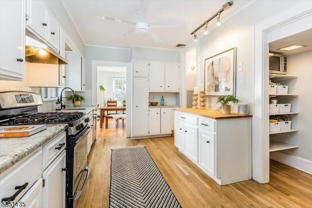 kitchen featuring ceiling fan, stainless steel range with gas stovetop, a sink, light wood finished floors, and white cabinetry