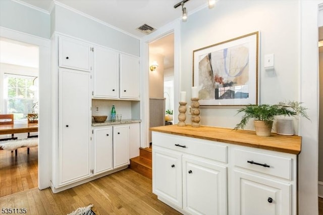 interior space with ornamental molding, light wood finished floors, white cabinetry, and wooden counters