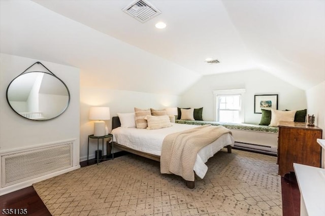 bedroom with a baseboard heating unit, visible vents, wood finished floors, and lofted ceiling