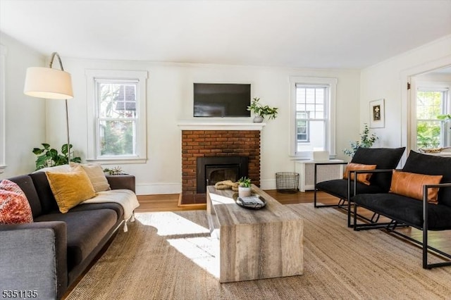 living room with a brick fireplace, a healthy amount of sunlight, radiator, and wood finished floors