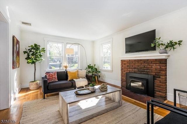 living room with baseboards, a brick fireplace, light wood-style flooring, and visible vents