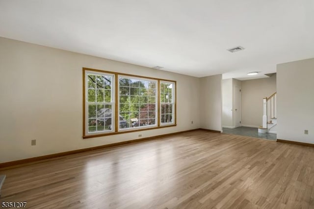 unfurnished living room featuring baseboards, wood finished floors, visible vents, and stairway