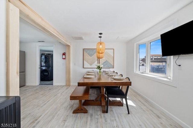 dining room with visible vents, stacked washer / drying machine, baseboards, and wood finished floors