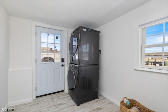 clothes washing area with baseboards, light wood-style floors, stacked washer / dryer, and laundry area