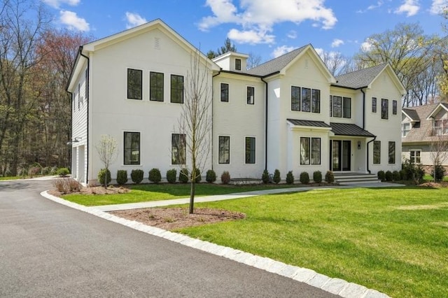 view of front of house with stucco siding, a front lawn, and a standing seam roof