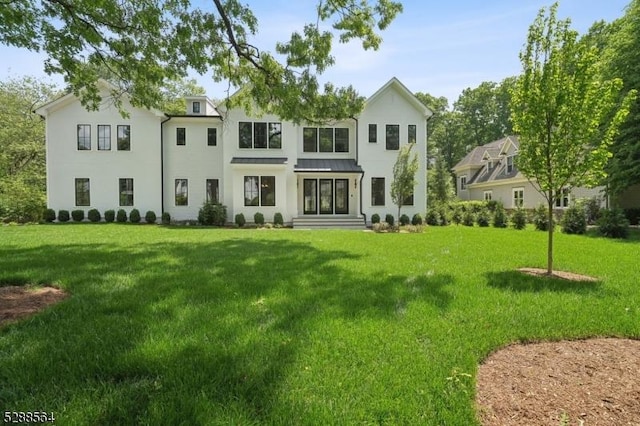 rear view of property featuring a standing seam roof, a yard, and stucco siding