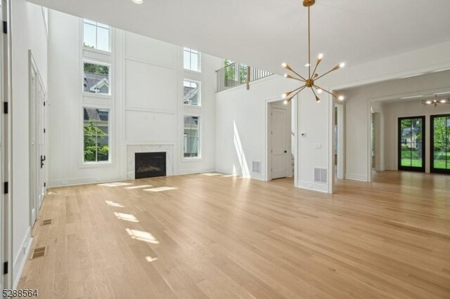 unfurnished living room with light wood-style floors, visible vents, baseboards, and an inviting chandelier