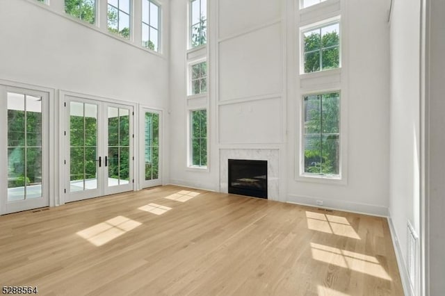 unfurnished living room with french doors, visible vents, wood finished floors, a high ceiling, and a fireplace