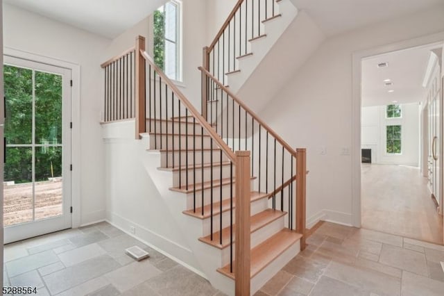 staircase featuring a fireplace, stone tile flooring, plenty of natural light, and baseboards