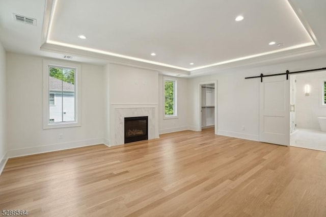 unfurnished living room with visible vents, plenty of natural light, a tray ceiling, and a barn door