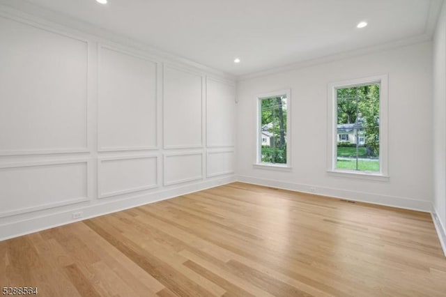 spare room featuring light wood-type flooring, a decorative wall, and ornamental molding