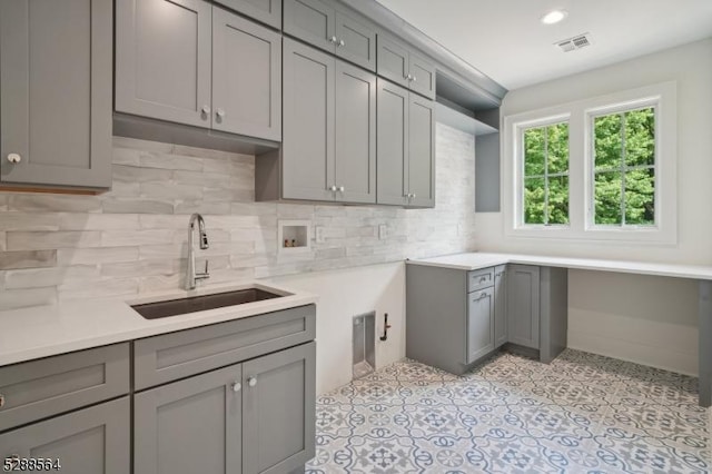 kitchen featuring visible vents, decorative backsplash, gray cabinetry, and a sink