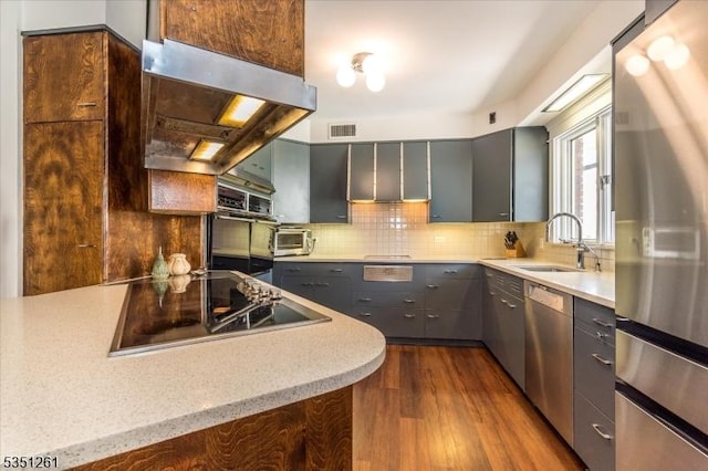 kitchen featuring a sink, extractor fan, appliances with stainless steel finishes, gray cabinetry, and visible vents