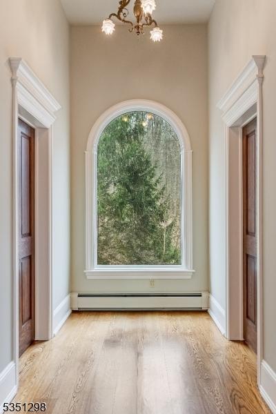 spare room with a chandelier, wood finished floors, baseboard heating, and baseboards