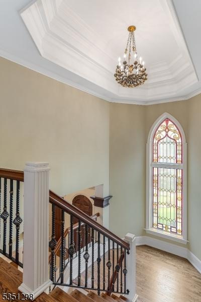 stairs with a chandelier, a tray ceiling, wood finished floors, crown molding, and baseboards
