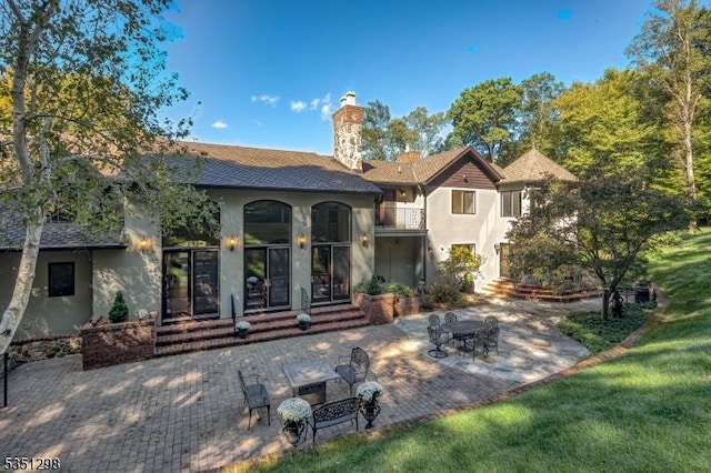 back of house with stucco siding, entry steps, a chimney, and a patio