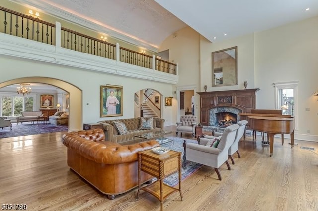 living room featuring arched walkways, a fireplace, a towering ceiling, wood finished floors, and stairway