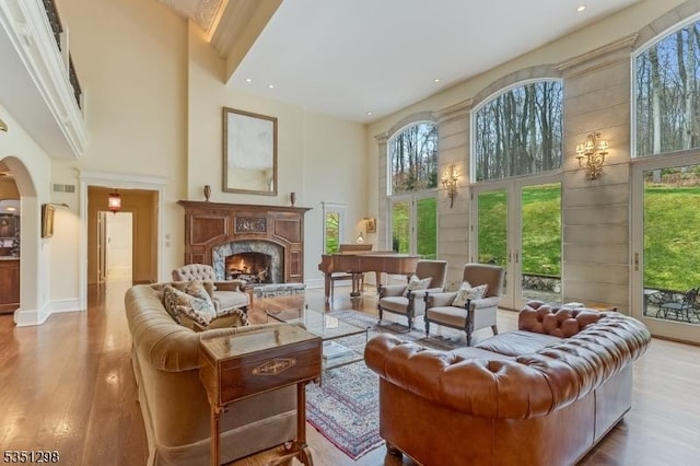living room with a high ceiling, healthy amount of natural light, a lit fireplace, wood finished floors, and arched walkways
