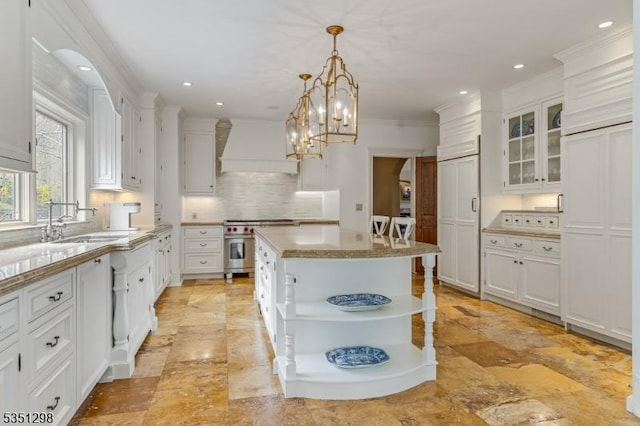 kitchen featuring premium range hood, a sink, high end range, decorative backsplash, and white cabinets
