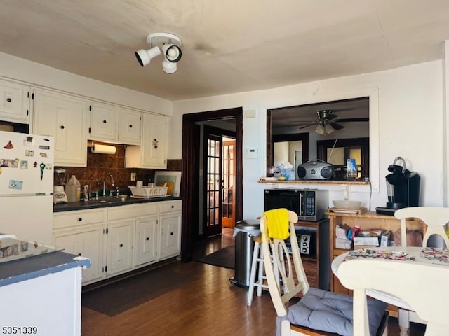 kitchen featuring freestanding refrigerator, dark countertops, a sink, dark wood-type flooring, and tasteful backsplash