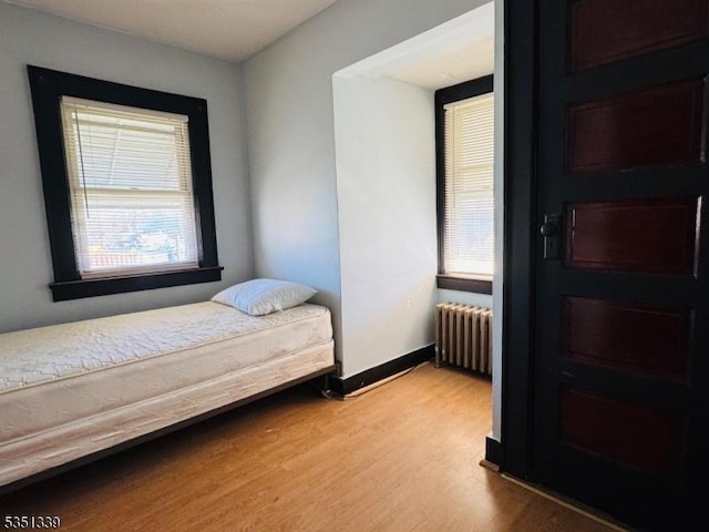 bedroom featuring radiator, light wood-style floors, and baseboards