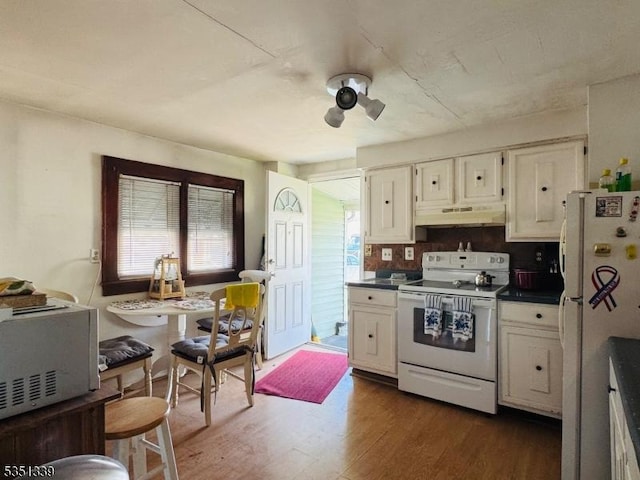 kitchen featuring white appliances, dark wood-type flooring, dark countertops, under cabinet range hood, and white cabinetry
