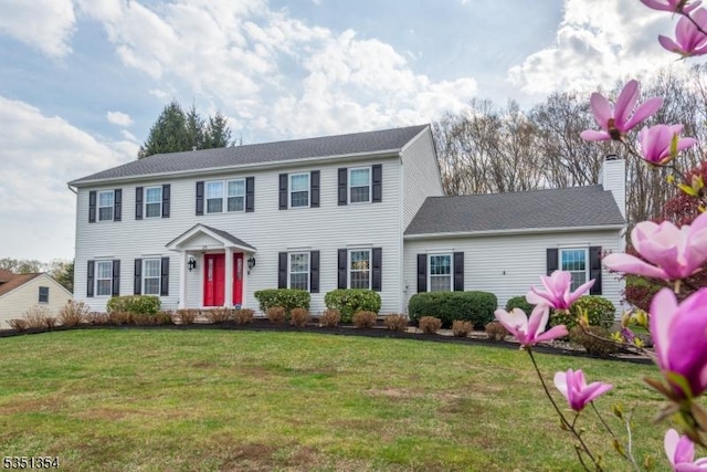 colonial inspired home featuring a chimney and a front lawn