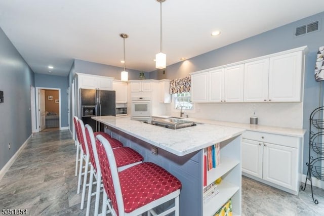 kitchen with a sink, black fridge with ice dispenser, a center island, white cabinetry, and baseboards