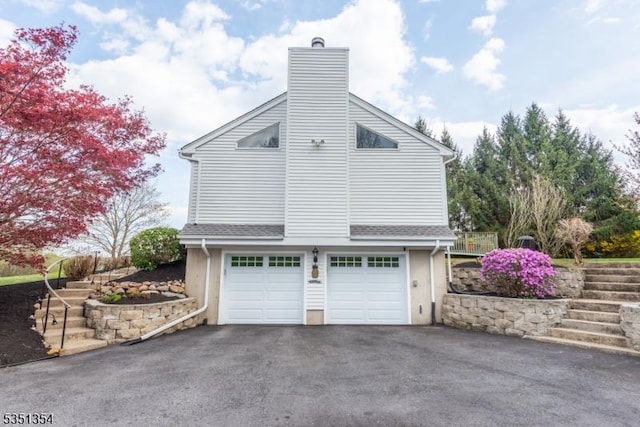 view of side of home featuring a chimney, aphalt driveway, an attached garage, and stairs