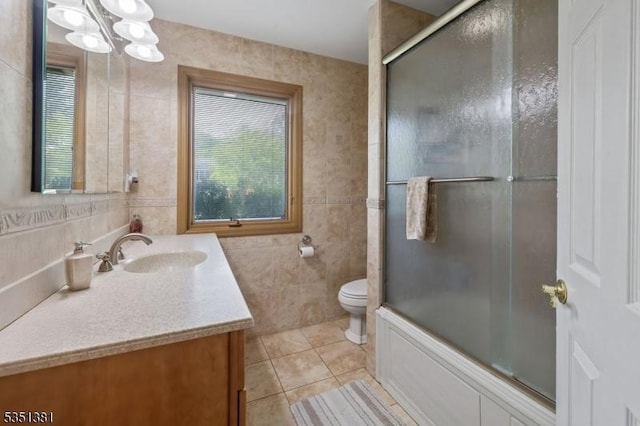 bathroom with an inviting chandelier, vanity, toilet, tile patterned floors, and tile walls