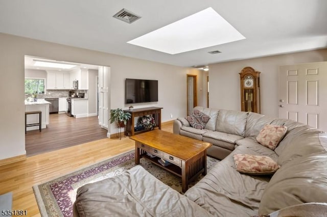 living room with visible vents, light wood finished floors, baseboards, and a skylight