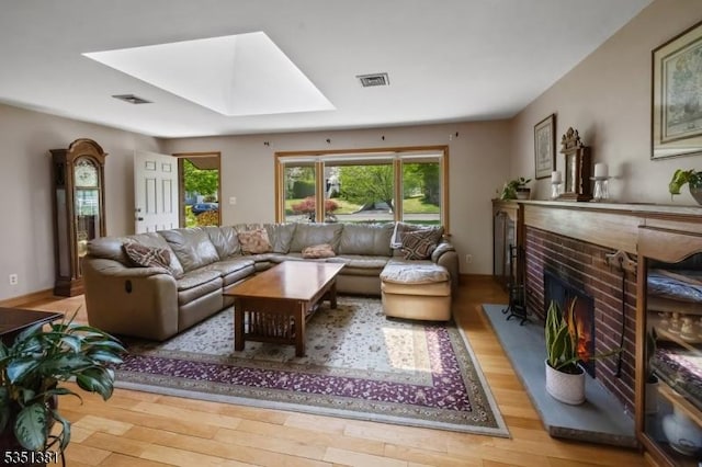living room with visible vents, a fireplace, wood finished floors, and a skylight