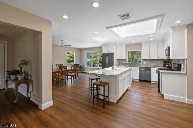 kitchen featuring appliances with stainless steel finishes, white cabinetry, decorative backsplash, a kitchen island, and visible vents