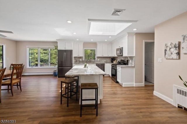 kitchen with black gas stove, baseboard heating, refrigerator, and a healthy amount of sunlight