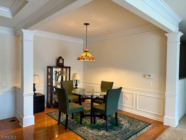 dining space with wood finished floors, wainscoting, ornamental molding, and decorative columns