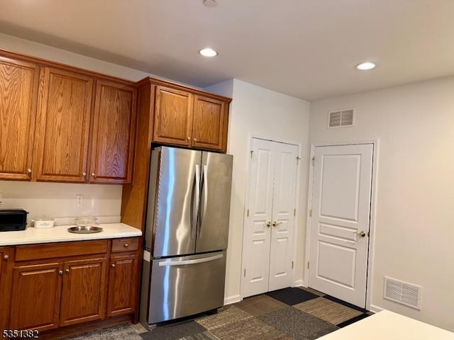 kitchen with visible vents, brown cabinetry, light countertops, and freestanding refrigerator