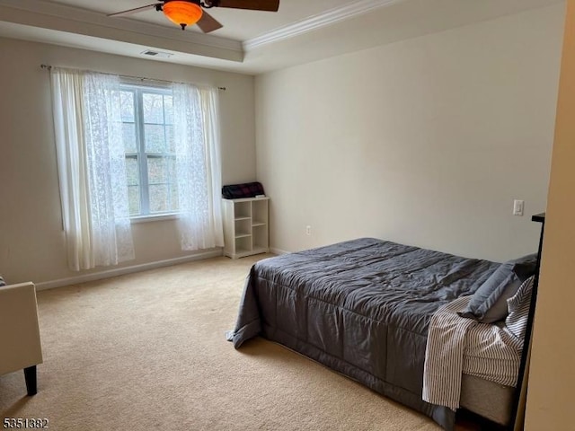 carpeted bedroom featuring a tray ceiling, baseboards, visible vents, a ceiling fan, and crown molding