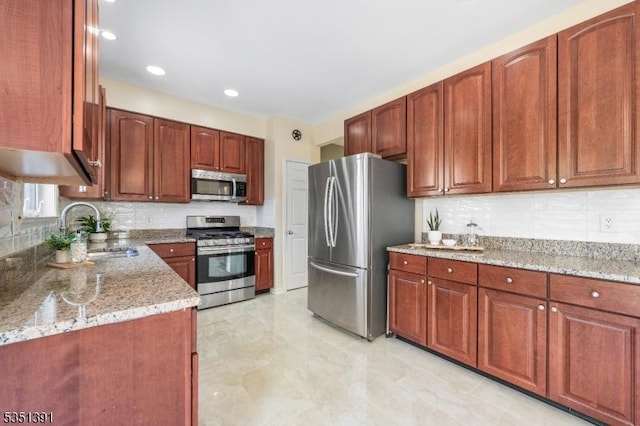 kitchen with backsplash, light stone countertops, appliances with stainless steel finishes, and a sink