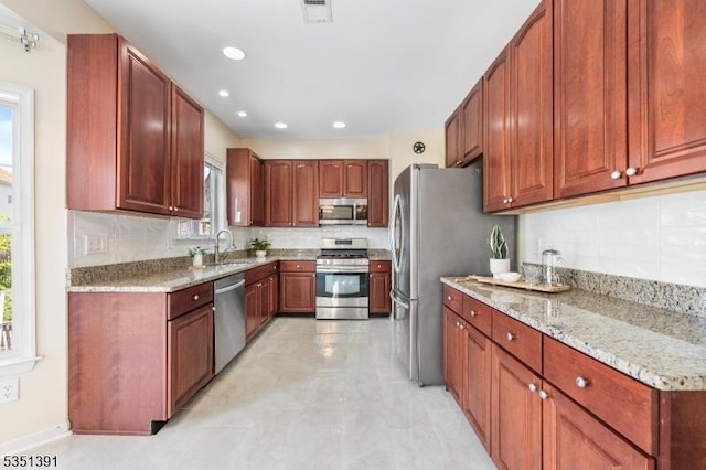 kitchen featuring appliances with stainless steel finishes, light stone counters, a sink, tasteful backsplash, and visible vents