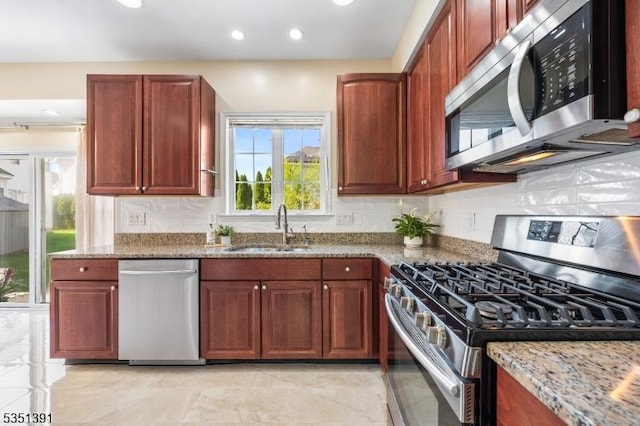kitchen with a sink, backsplash, light stone countertops, and stainless steel appliances