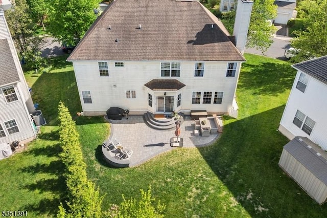 back of house with a lawn, a patio area, roof with shingles, and a chimney